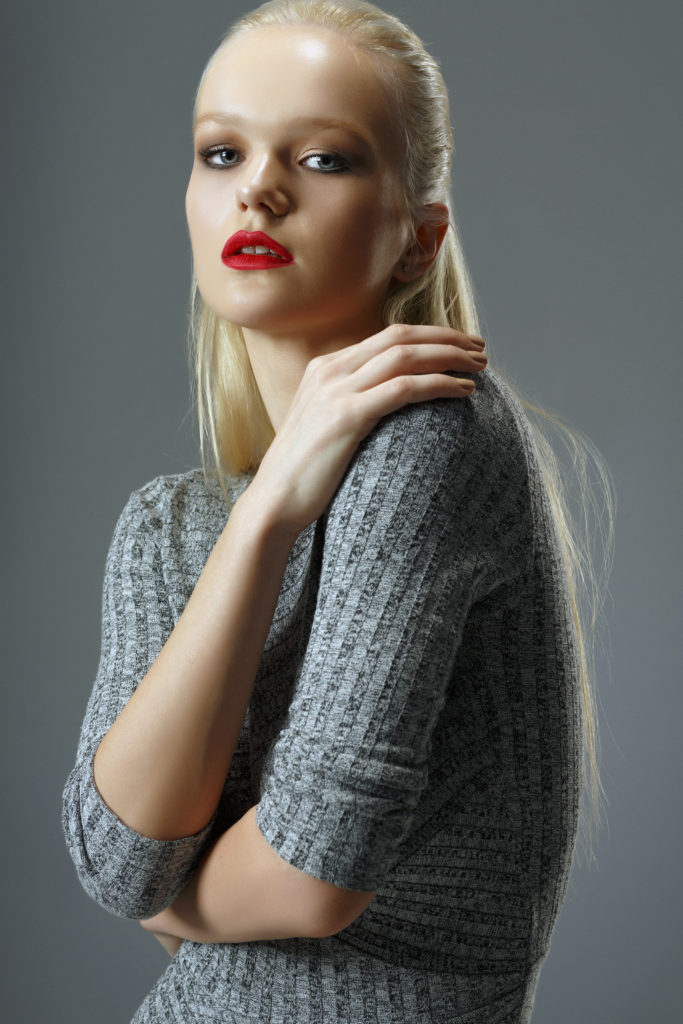 Beauty, fashion portrait. Original looks. Beautiful, lovely  and sensual young girl.  Hair back, blonde women, dressed elegantly.  Wearing a gray dress. Gray wall background. Developed from RAW, Adobe RGB color profile.